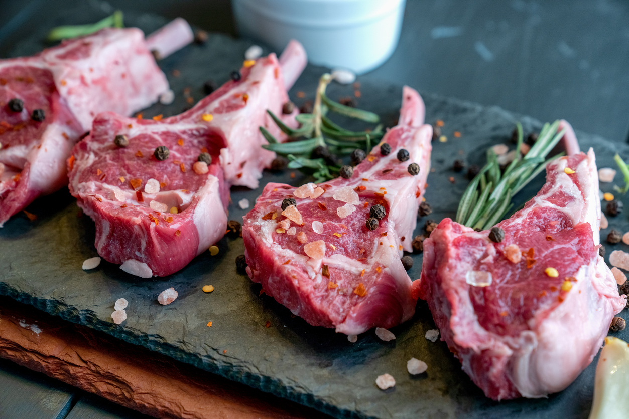 Raw Lamb Chops Prepared on a Dark Slate Cutting Board with a Ramekin or Pesto on the side with Rosemary and other herbs