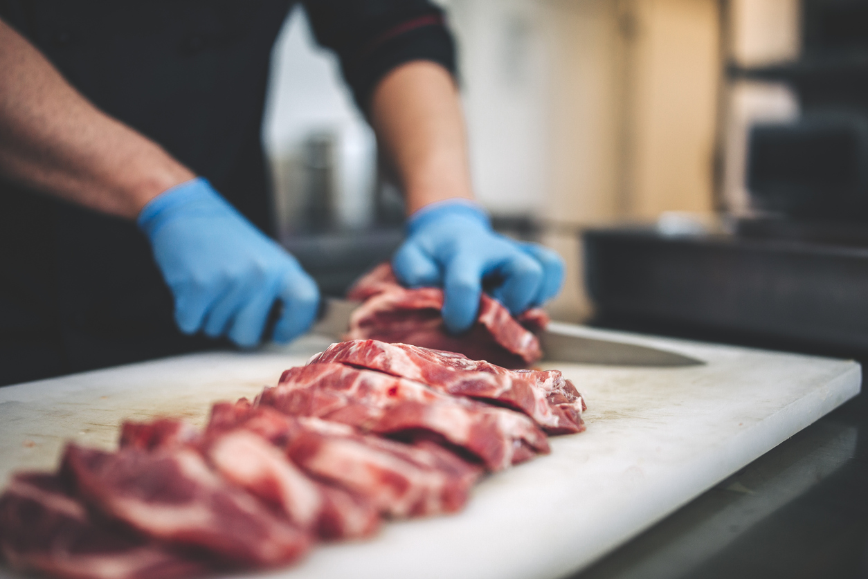 Male butcher cut raw meat with sharp knife in restaurants kitchen