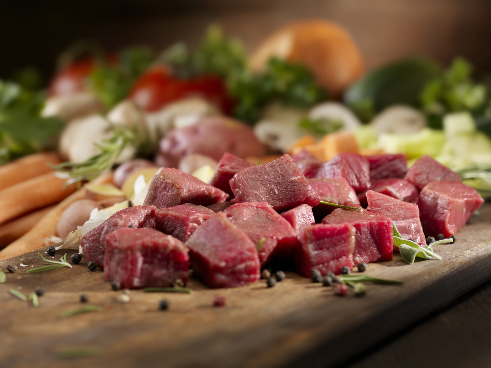 Pieces of raw meat on cutting board with vegetables in background